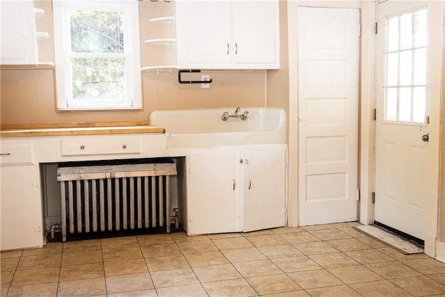 laundry room with radiator, plenty of natural light, light tile patterned flooring, and a sink
