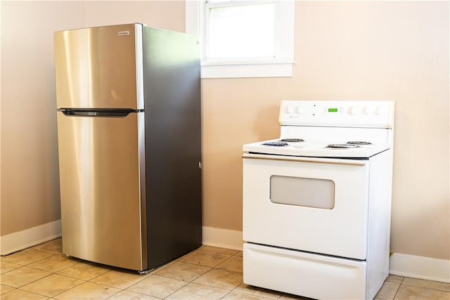 kitchen with freestanding refrigerator, white range with electric cooktop, baseboards, white cabinets, and light tile patterned flooring