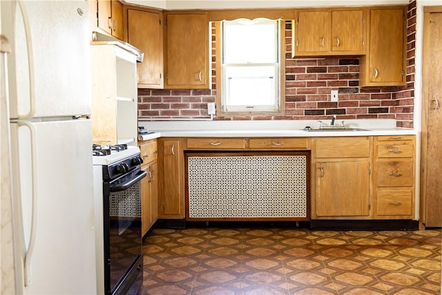 kitchen featuring freestanding refrigerator, gas stove, light countertops, a sink, and brown cabinetry