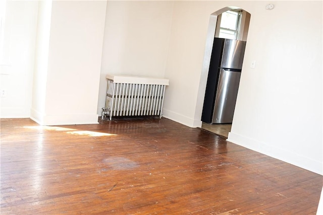 empty room featuring radiator, arched walkways, baseboards, and hardwood / wood-style flooring