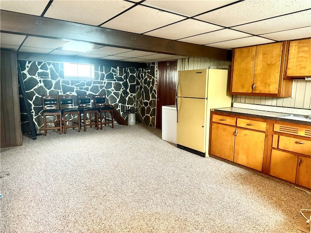 below grade area featuring freestanding refrigerator, a paneled ceiling, refrigerator, a sink, and wood walls