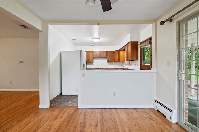 kitchen with baseboard heating, white refrigerator with ice dispenser, brown cabinets, light wood-style floors, and a ceiling fan