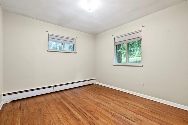 spare room featuring baseboard heating, plenty of natural light, light wood-style floors, and baseboards