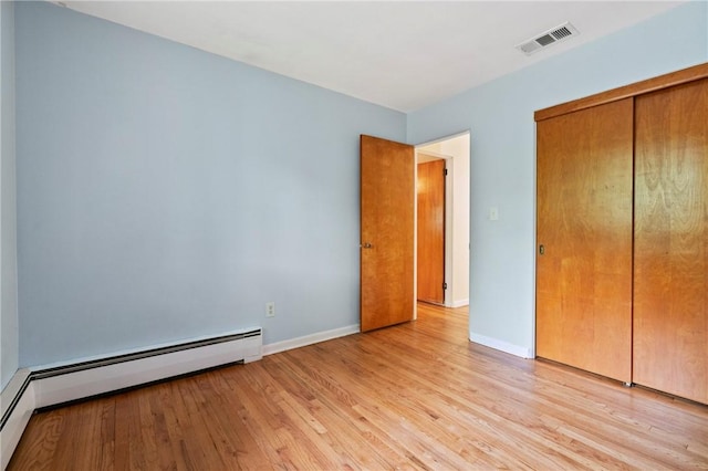 unfurnished bedroom with a baseboard heating unit, light wood-style floors, baseboards, and a closet