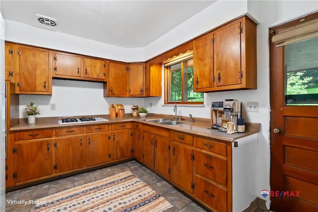 kitchen with a sink, white gas stovetop, brown cabinets, and healthy amount of natural light