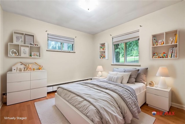 bedroom featuring baseboard heating, wood finished floors, and multiple windows
