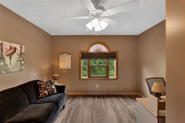 living area with wood finished floors, ceiling fan, a textured ceiling, and baseboards