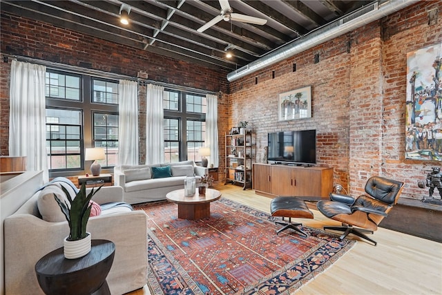living area featuring brick wall, a high ceiling, wood finished floors, track lighting, and a ceiling fan