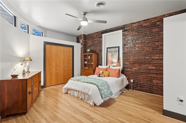 bedroom with brick wall, light wood-style floors, a closet, and ceiling fan
