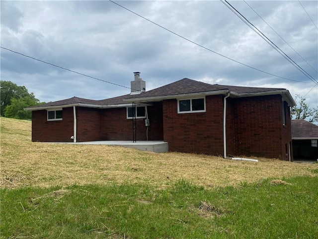 rear view of house with brick siding, a chimney, and a lawn