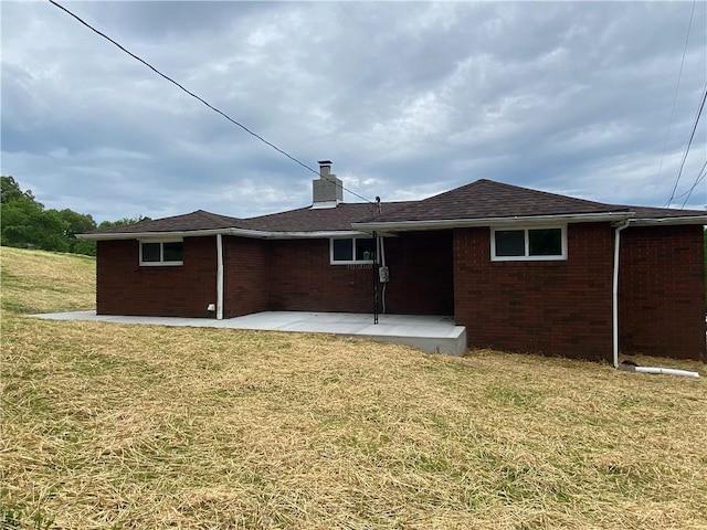 back of property with a patio area, brick siding, a yard, and a chimney