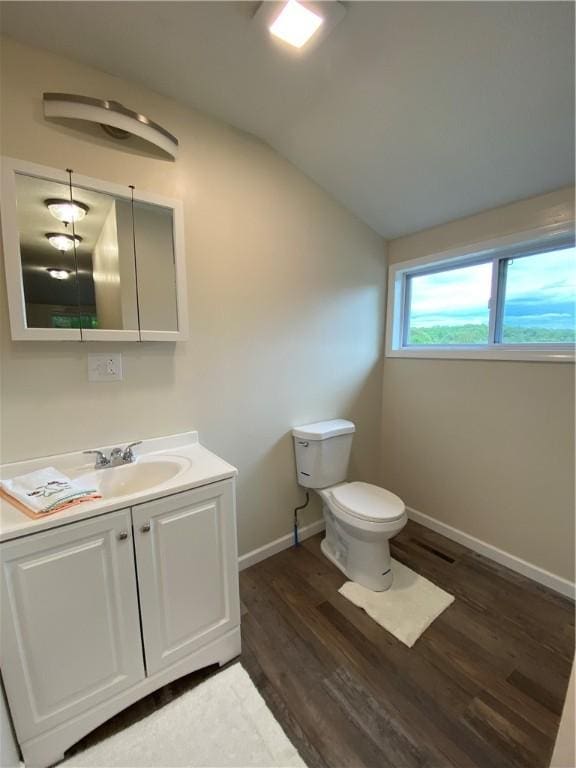 half bathroom featuring wood finished floors, vaulted ceiling, toilet, vanity, and baseboards