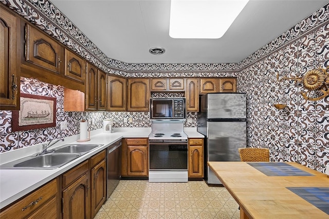 kitchen featuring stainless steel appliances, a sink, light floors, light countertops, and wallpapered walls