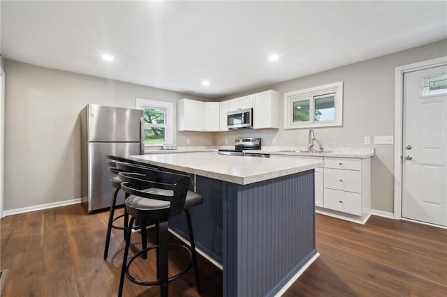 kitchen with stainless steel appliances, a center island, baseboards, white cabinetry, and recessed lighting