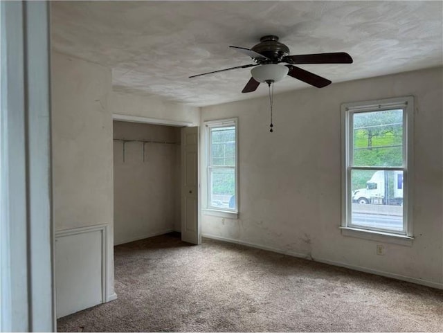 unfurnished bedroom featuring multiple windows, carpet, a closet, and a ceiling fan