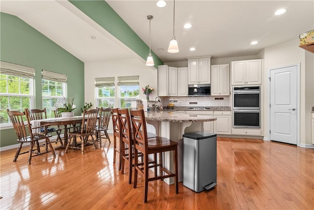 kitchen with stainless steel appliances, a kitchen bar, white cabinets, tasteful backsplash, and light wood-style floors