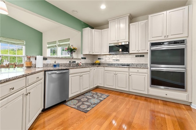 kitchen featuring appliances with stainless steel finishes, a sink, white cabinets, tasteful backsplash, and light wood-style flooring
