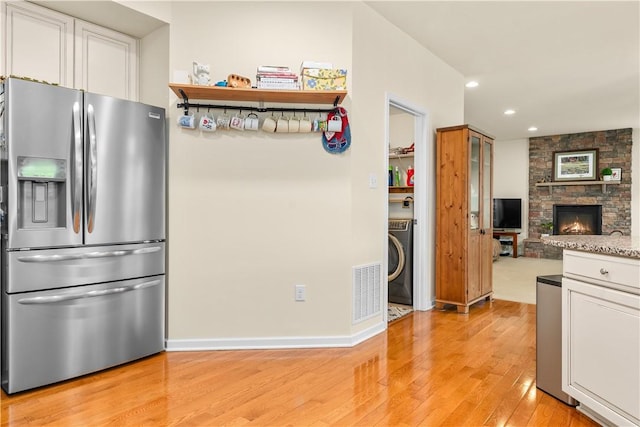 kitchen with stainless steel refrigerator with ice dispenser, washer / clothes dryer, light wood-style floors, white cabinets, and recessed lighting