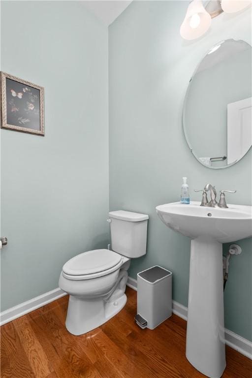 half bathroom featuring wood finished floors, toilet, and baseboards