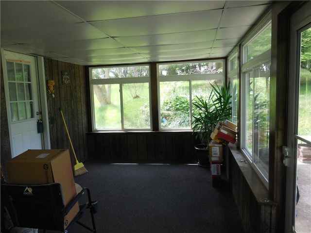 sunroom featuring carpet floors, wooden walls, healthy amount of natural light, and a drop ceiling