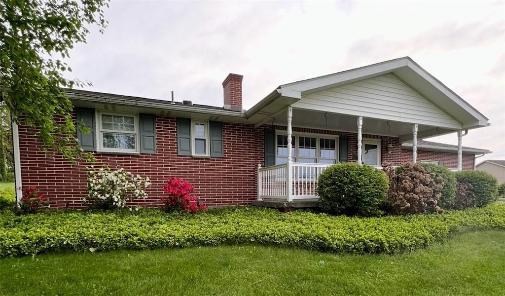 view of front of house featuring a chimney, brick siding, and a porch