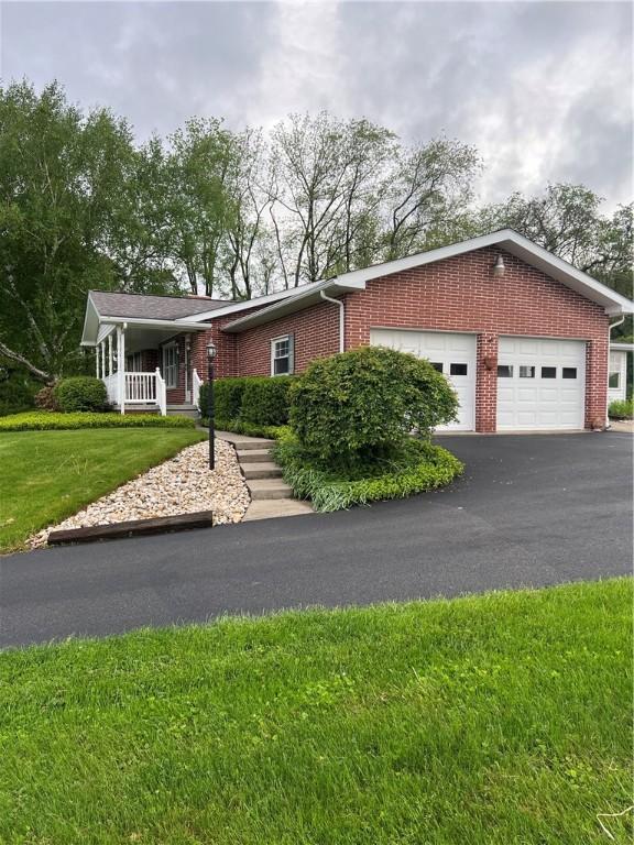 single story home with brick siding, a garage, a front lawn, driveway, and a porch