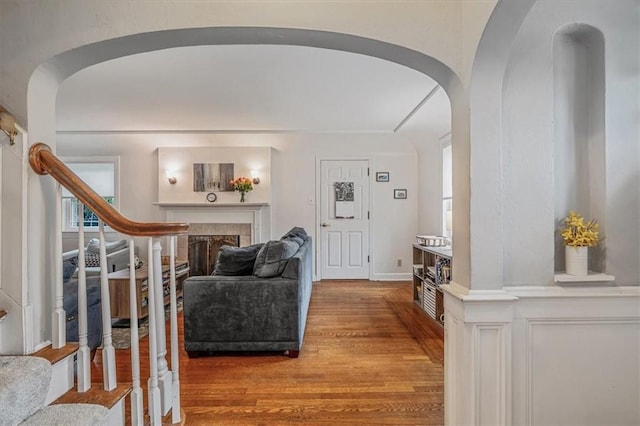 entryway with wood finished floors, arched walkways, a tile fireplace, and stairway