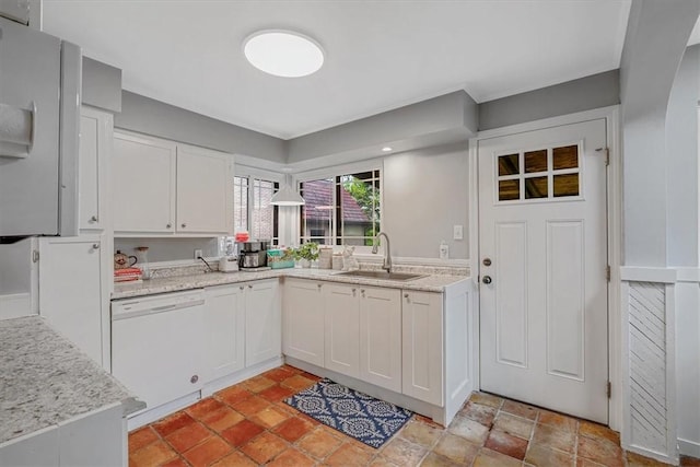 kitchen with a sink, white dishwasher, white cabinetry, and light stone counters