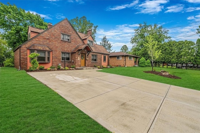 english style home featuring a chimney, a front yard, brick siding, and concrete driveway