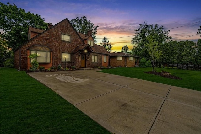 english style home with a chimney, a front lawn, and brick siding
