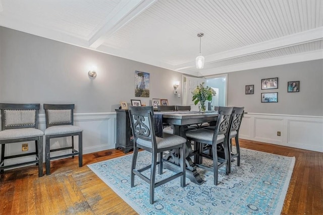 dining area featuring beamed ceiling, hardwood / wood-style floors, a wainscoted wall, and a decorative wall