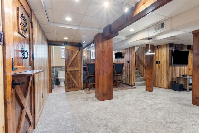 below grade area featuring a barn door, wooden walls, stairway, carpet flooring, and recessed lighting