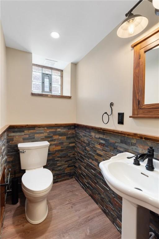 bathroom featuring wainscoting, wood finished floors, toilet, a sink, and tile walls