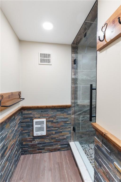 full bath featuring a shower stall, wood finished floors, and heating unit