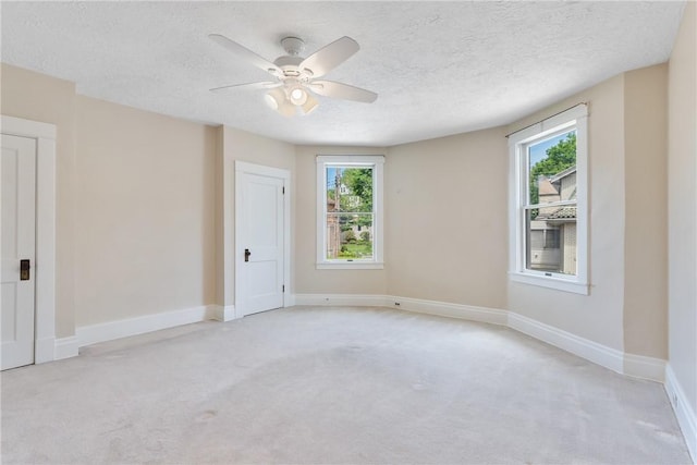empty room featuring light colored carpet, ceiling fan, a textured ceiling, and baseboards