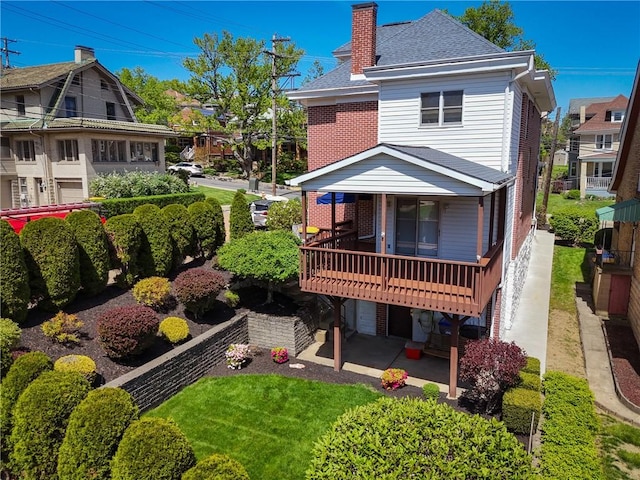 rear view of property with brick siding, roof with shingles, a chimney, and a patio area