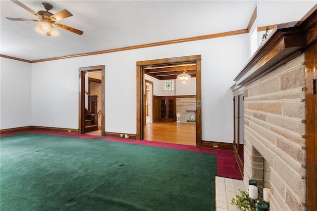spare room featuring a brick fireplace, ornamental molding, baseboards, a ceiling fan, and stairs