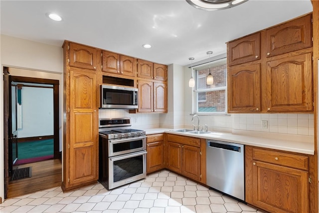 kitchen featuring stainless steel appliances, a sink, brown cabinetry, light countertops, and tasteful backsplash