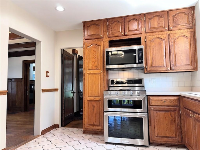 kitchen with appliances with stainless steel finishes, light countertops, brown cabinetry, decorative backsplash, and recessed lighting
