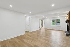 unfurnished living room with a fireplace with flush hearth, recessed lighting, light wood-style flooring, and baseboards