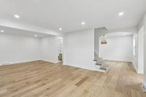 basement with recessed lighting, arched walkways, wood finished floors, stairway, and baseboards
