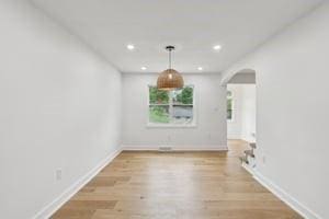 unfurnished dining area featuring arched walkways, baseboards, recessed lighting, and wood finished floors