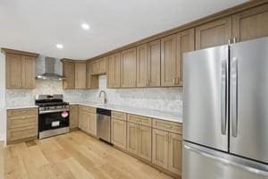 kitchen featuring stainless steel appliances, wall chimney range hood, light countertops, decorative backsplash, and light wood-style flooring