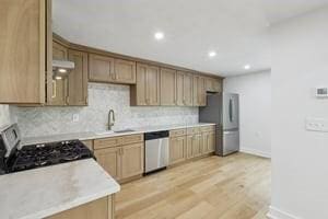 kitchen featuring a sink, appliances with stainless steel finishes, baseboards, tasteful backsplash, and light countertops