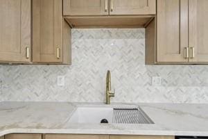 kitchen featuring a sink, backsplash, and light stone counters