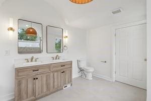 bathroom with toilet, double vanity, and baseboards