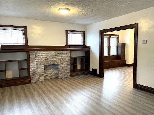 unfurnished living room with wood finished floors, a textured ceiling, baseboards, and a fireplace