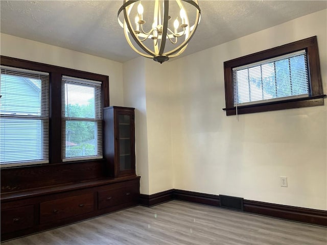 unfurnished room with light wood-style floors, a chandelier, baseboards, and a textured ceiling