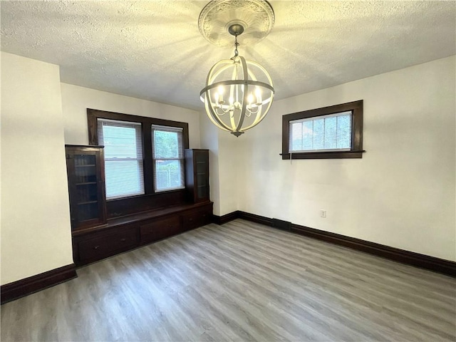 empty room featuring a chandelier, wood finished floors, baseboards, and a textured ceiling
