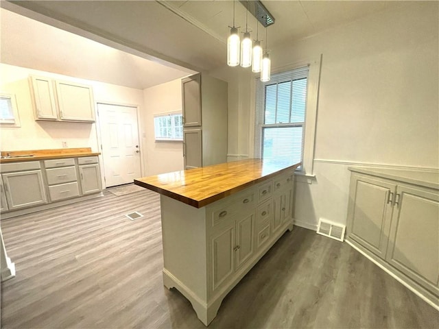 kitchen with butcher block countertops, wood finished floors, a peninsula, pendant lighting, and baseboards
